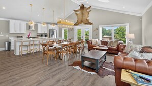 A spacious living area with a large brown leather couch, a wooden coffee table, and a dining area with wooden chairs and a white island.