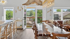 Un comedor amplio con una larga mesa de madera y sillas, un techo con un gran felpudo de piel, y vistas a un paisaje verde exuberante a través de puertas abiertas.