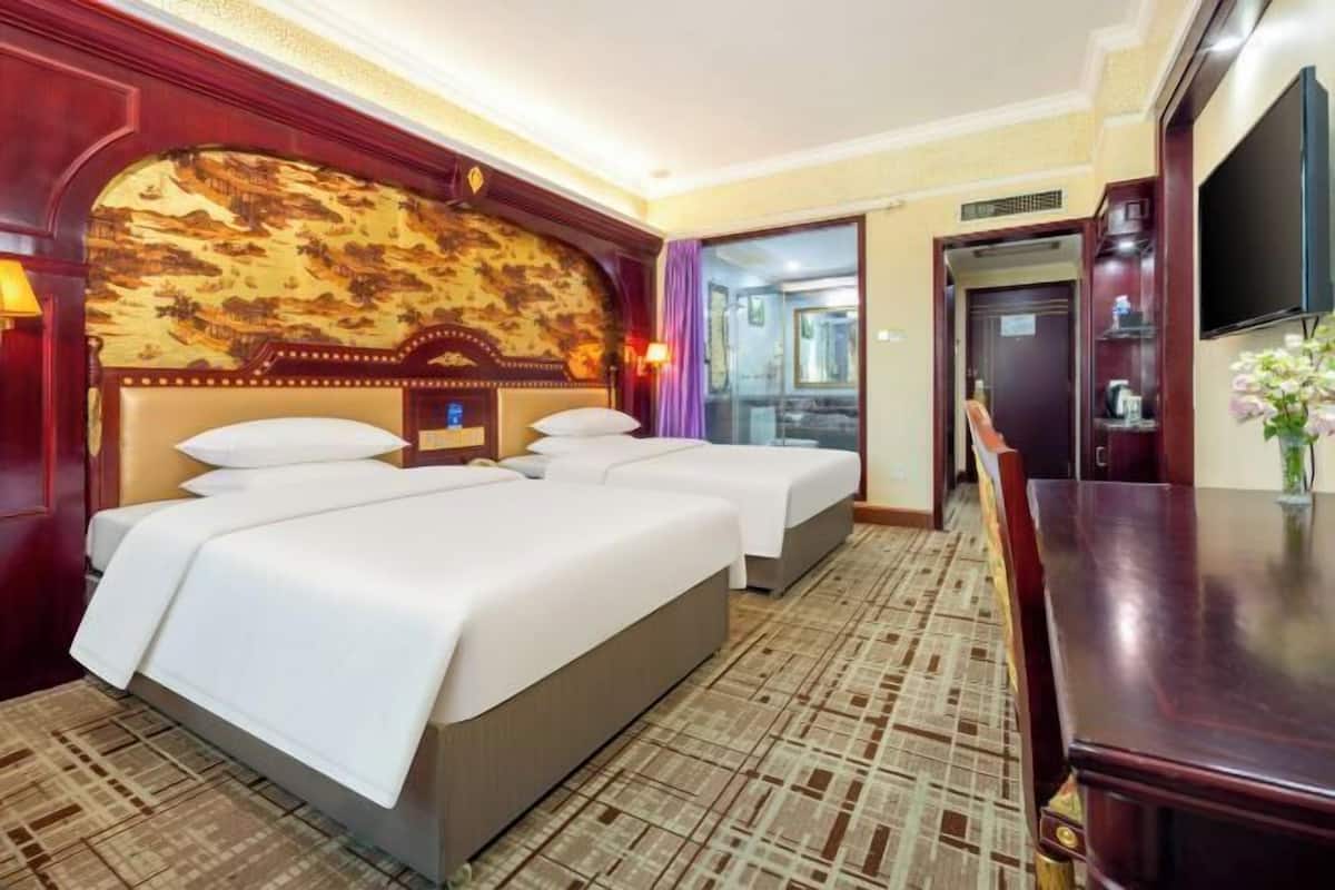 Ein Hotelzimmer mit einem großen Bett, einem Schreibtisch, einem Fernseher und einem durch eine Glastür einsehbaren Badezimmer.