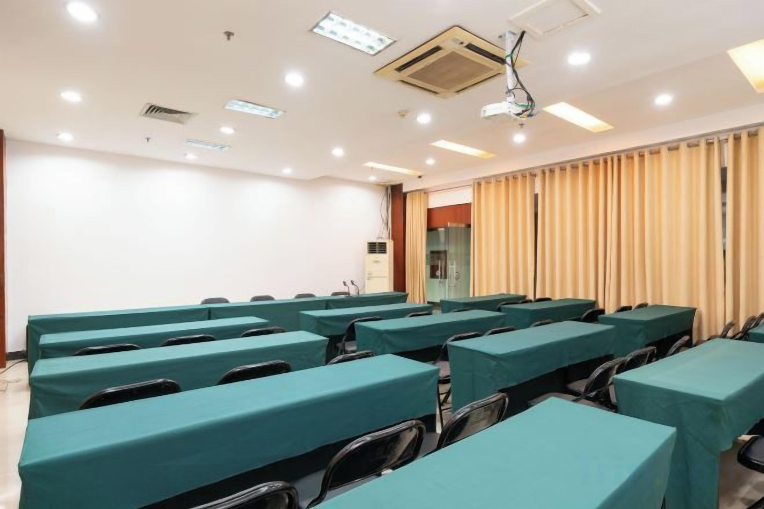 A conference room with rows of tables and chairs, a projector, and a window with curtains.