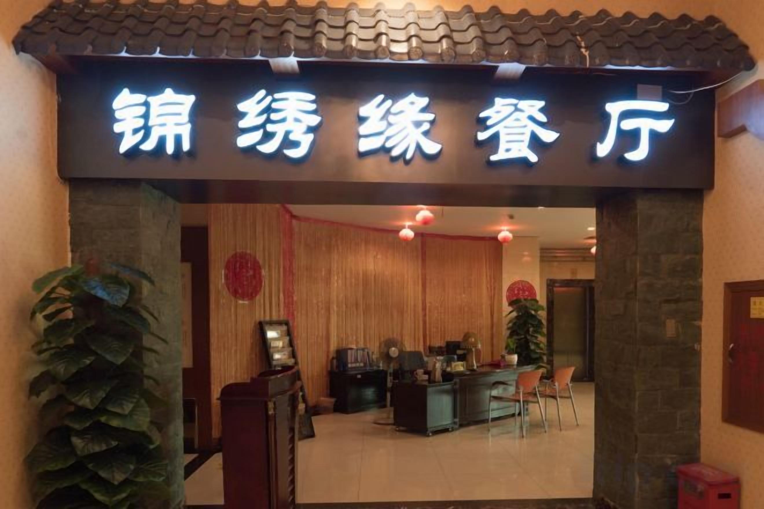 A hotel entrance with a sign in a foreign language, a reception desk, and a seating area.