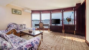 A living room with a sofa, a coffee table, and a TV on a balcony with a view. - Hengsheng Hotel (Baise)