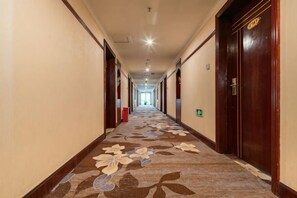 A hotel corridor with a patterned carpet, wooden doors, and a long hallway leading to a bright room at the end. - Hengsheng Hotel (Baise)