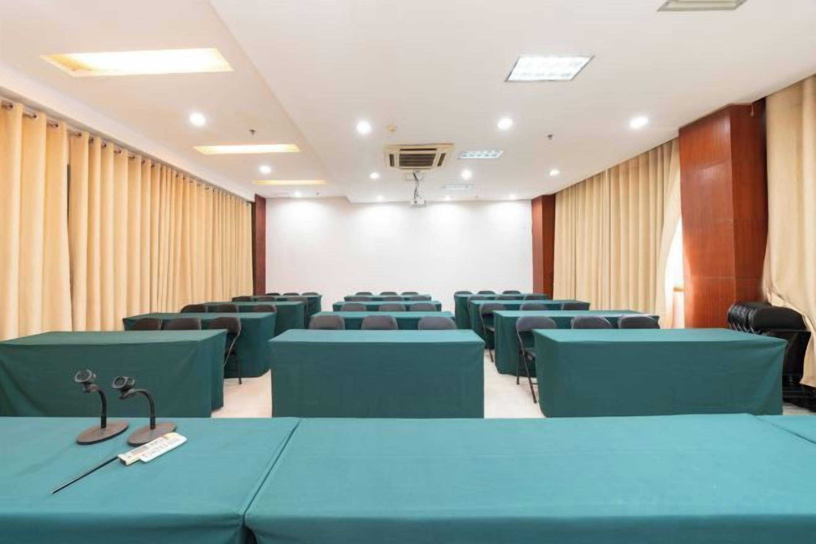A conference room with rows of tables and chairs, a podium, and a large window with curtains.