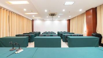 A conference room with rows of tables and chairs, a podium, and a large window with curtains.
