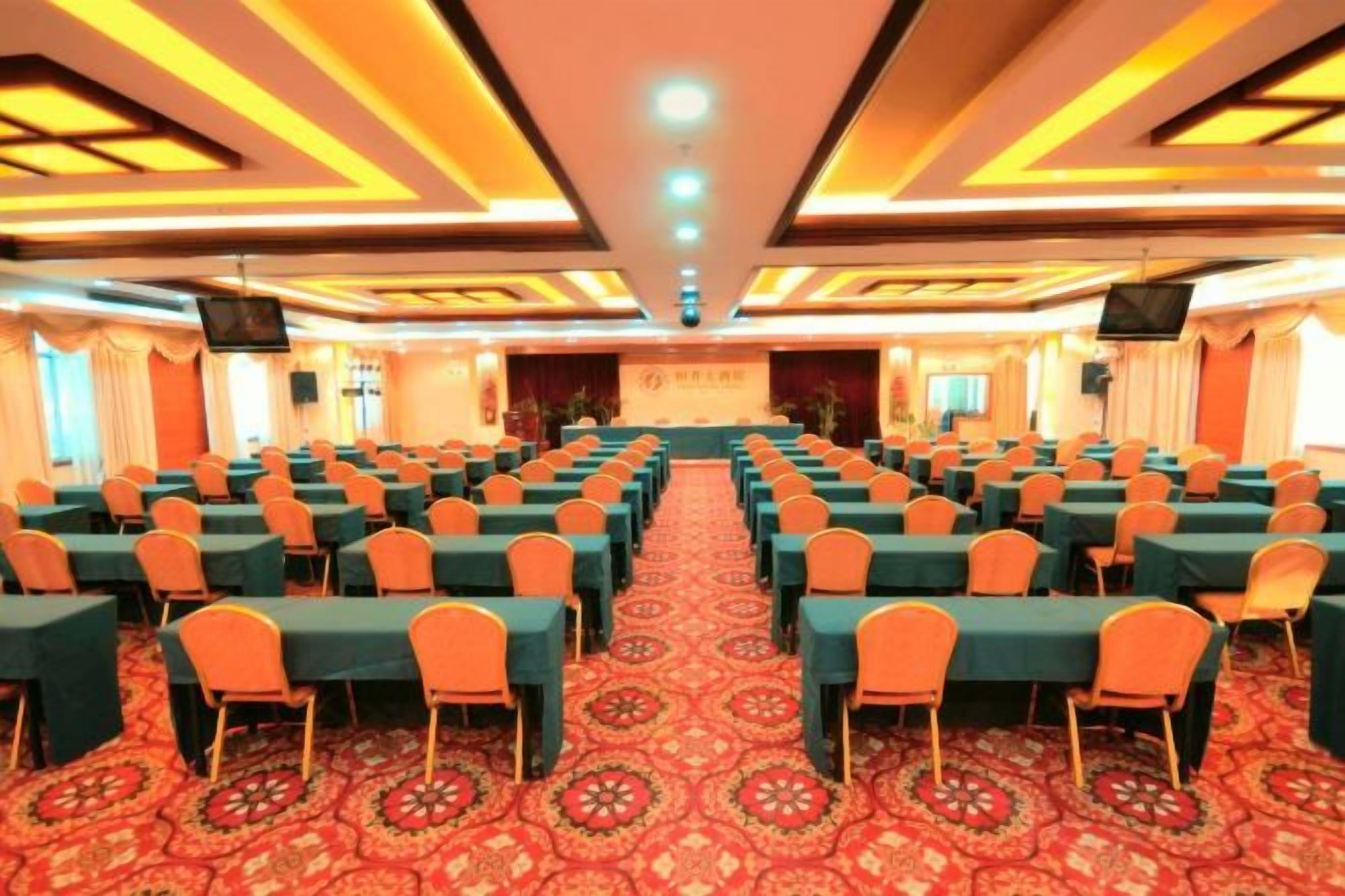 A conference room with rows of tables and chairs, a carpeted floor, and a stage at the front.