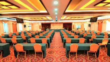 A conference room with rows of tables and chairs, a carpeted floor, and a stage at the front.