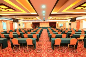 A conference room with rows of tables and chairs, a carpeted floor, and a stage at the front.