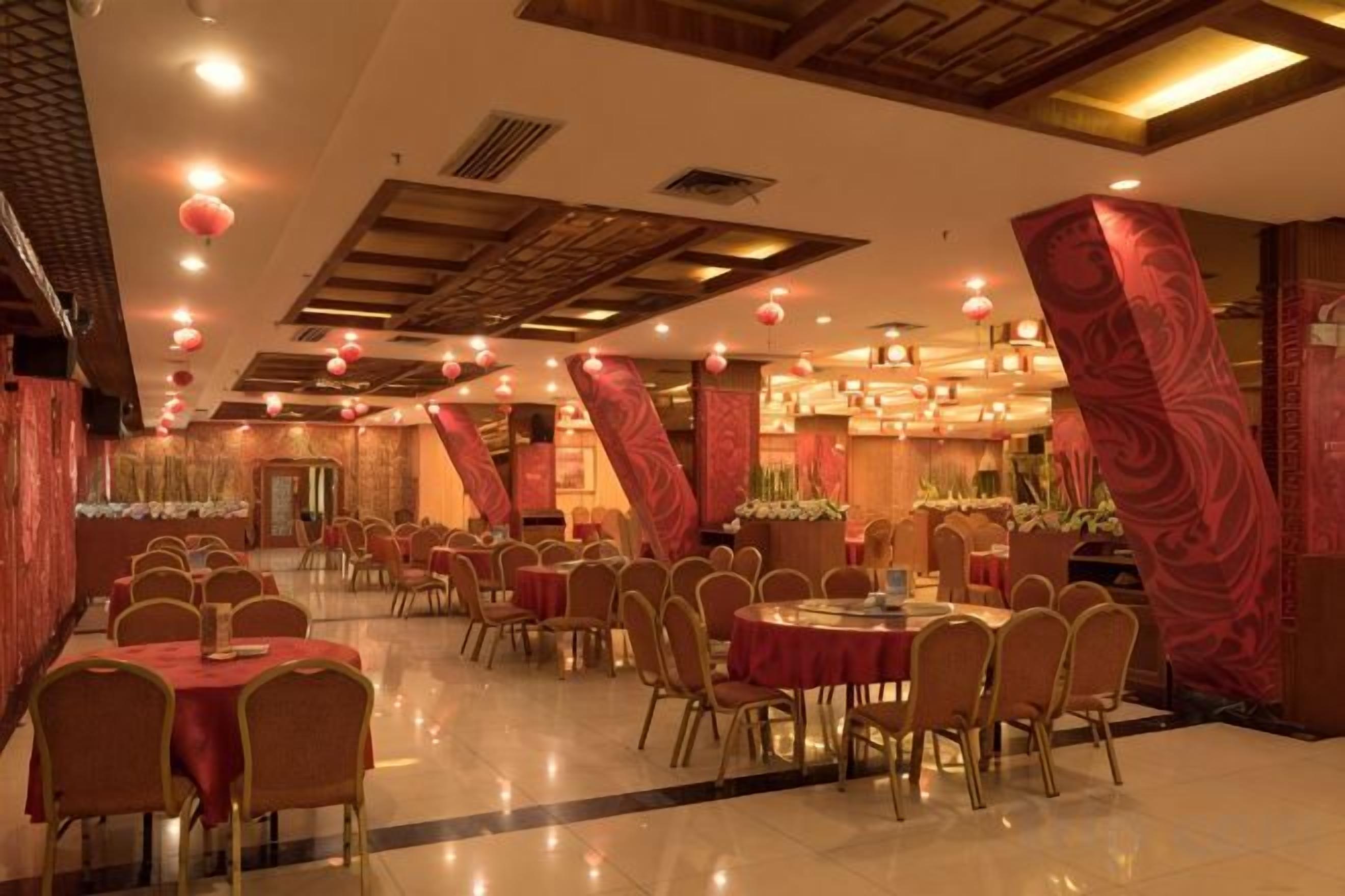 A banquet hall with round tables and chairs, red drapery, and a modern ceiling design.