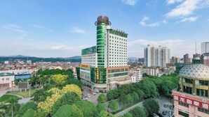 A high-rise hotel with a green and white facade, surrounded by trees and other buildings. - Hengsheng Hotel (Baise)