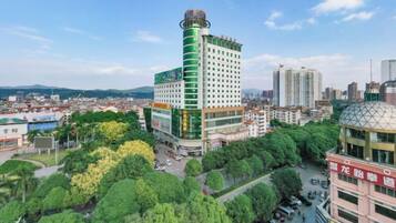 A high-rise building with a green and white facade, surrounded by trees and other buildings.