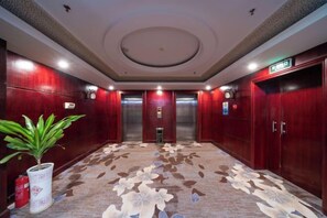 A hotel lobby with a patterned carpet, wooden walls, and two elevators. - Hengsheng Hotel (Baise)