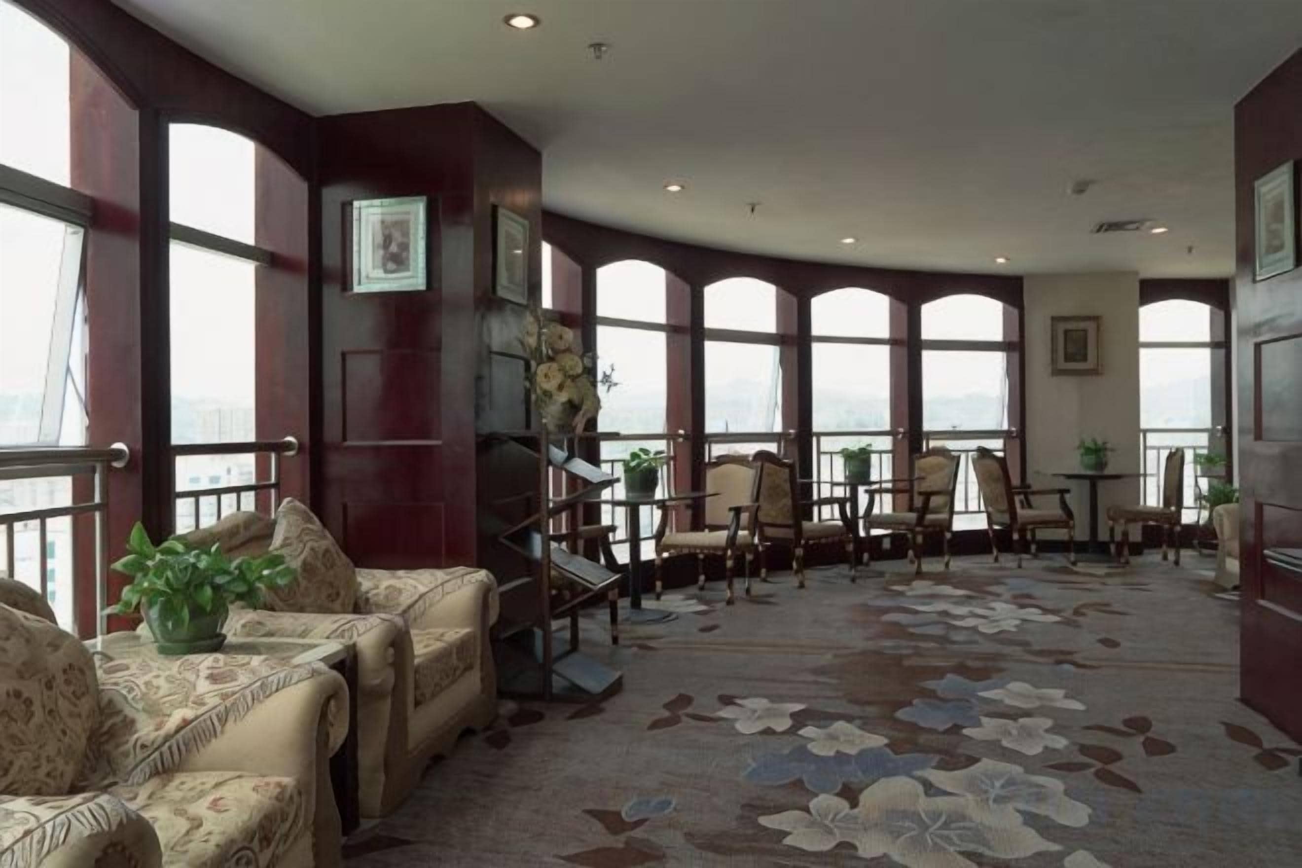 Un salon spacieux doté d’une grande fenêtre, d’un tapis à motifs et d’un coin salon avec des canapés et des fauteuils.