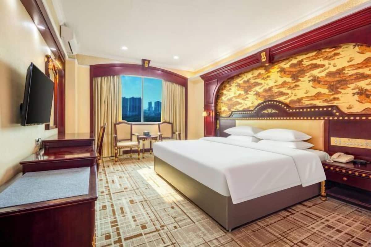 Ein Hotelzimmer mit einem großen Bett, einem Schreibtisch, einem Sessel, einem Fernseher und Blick auf die Stadt.
