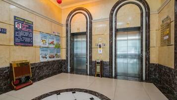 A lobby with two elevators, a reception desk, and informational posters on the walls.