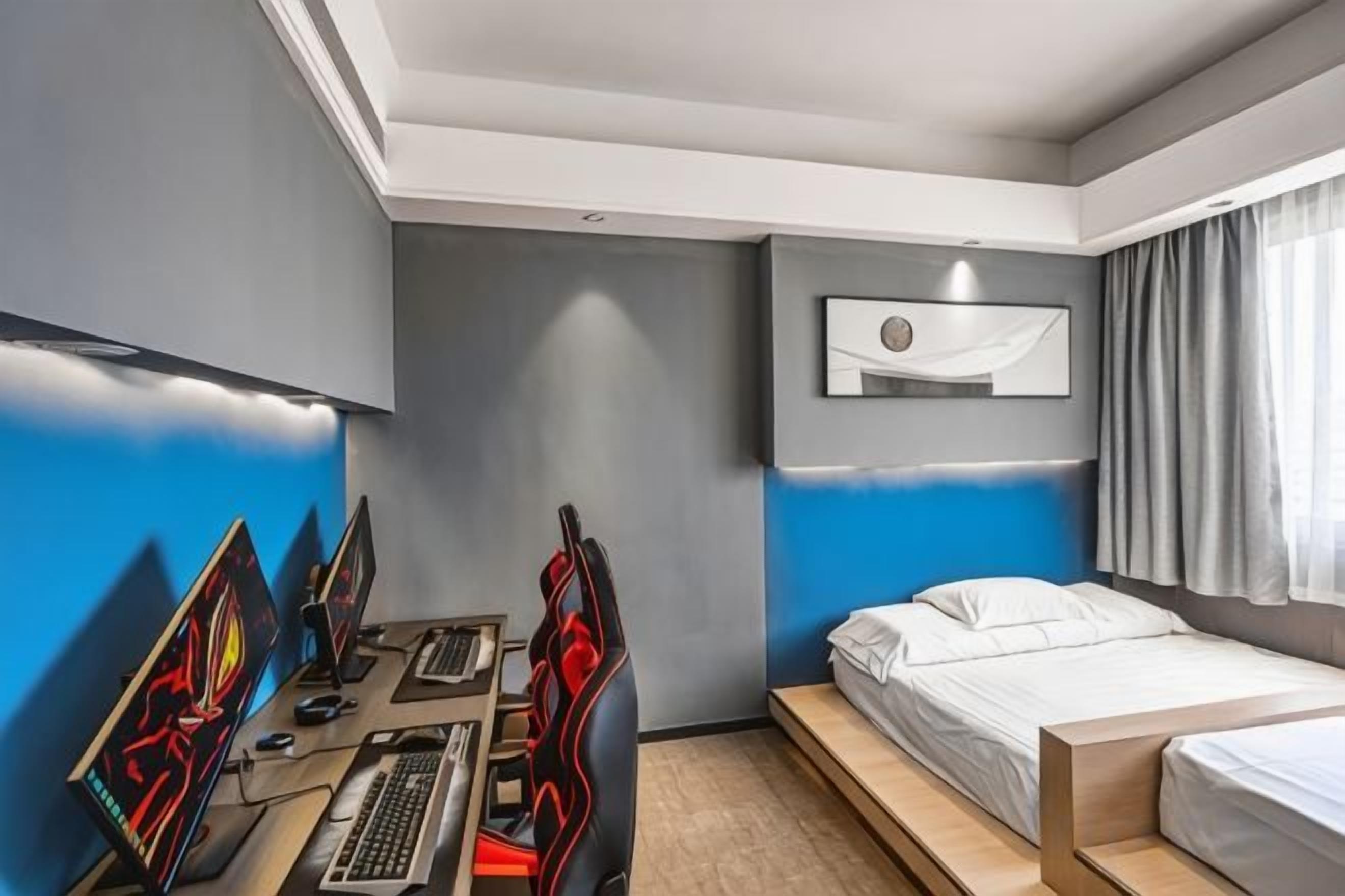 Una habitación de hotel moderna con escritorio, múltiples monitores, una cama y un amplio ventanal.