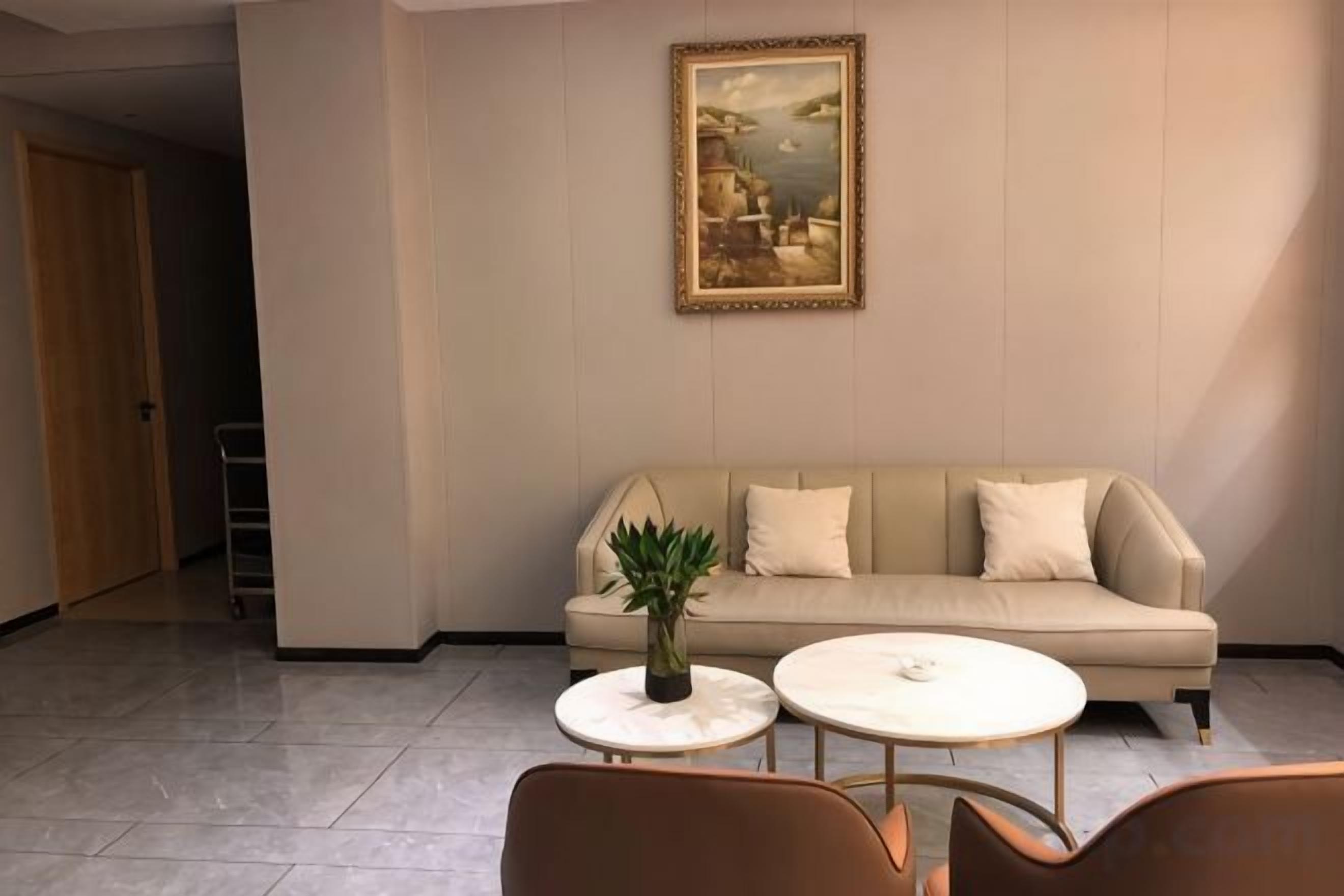 A room with a beige sofa, two round tables, and a potted plant.