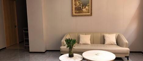 A room with a beige sofa, two round tables, and a potted plant.