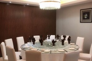 Un salón de conferencias con una mesa redonda de vidrio, sillas blancas y una lámpara de araña.