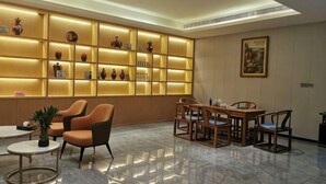 Una hall d'albergo con un'area salotto, una parete con scaffali illuminati e un tavolo da pranzo.