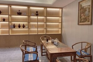 A dining area with a wooden table and chairs, a wall with illuminated shelves, and a framed painting on the wall.