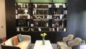 Un'area living moderna con un divano, poltrone, un tavolino da caffè e un'ampia libreria piena di libri e oggetti decorativi.