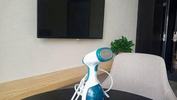 Quarto com mesa, secador elétrico azul e branco, planta em vaso e televisão de tela plana fixada na parede.