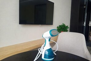 A room with a table, a blue and white electric hairdryer, a potted plant, and a flat-screen TV mounted on the wall. - Hengtai Hotel (Zhengzhou Zijingshan Street Subway Station) (Zhengzhou)