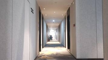 A long, narrow hotel corridor with a patterned carpet, walls with a textured finish, and a ceiling with recessed lighting.