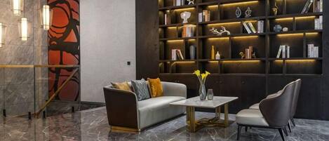 A modern lobby with a marble floor, a sofa, a coffee table, a bookshelf, and a decorative wall.