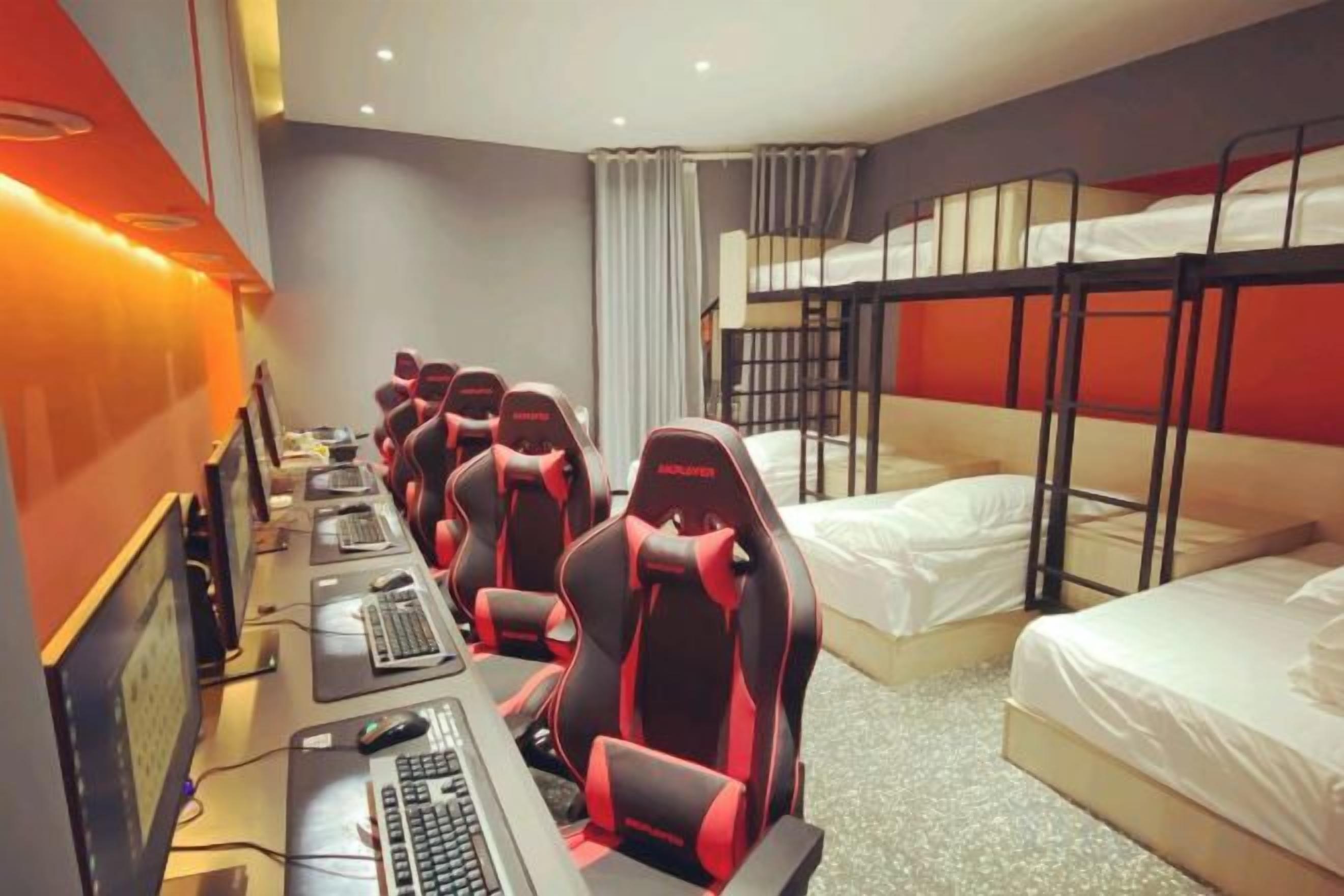 A hotel room with bunk beds, a desk with multiple computers, and a row of gaming chairs.