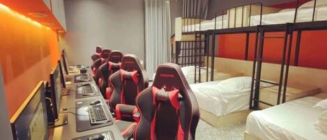 A hotel room with bunk beds, a desk with multiple computers, and a row of gaming chairs.