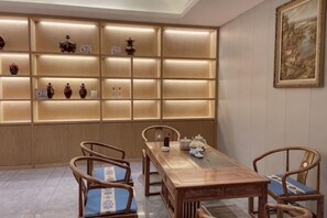 A dining area with a wooden table and chairs, a wall with illuminated shelves, and a framed painting. - Hengtai Hotel (Zhengzhou Zijingshan Street Subway Station) (Zhengzhou)
