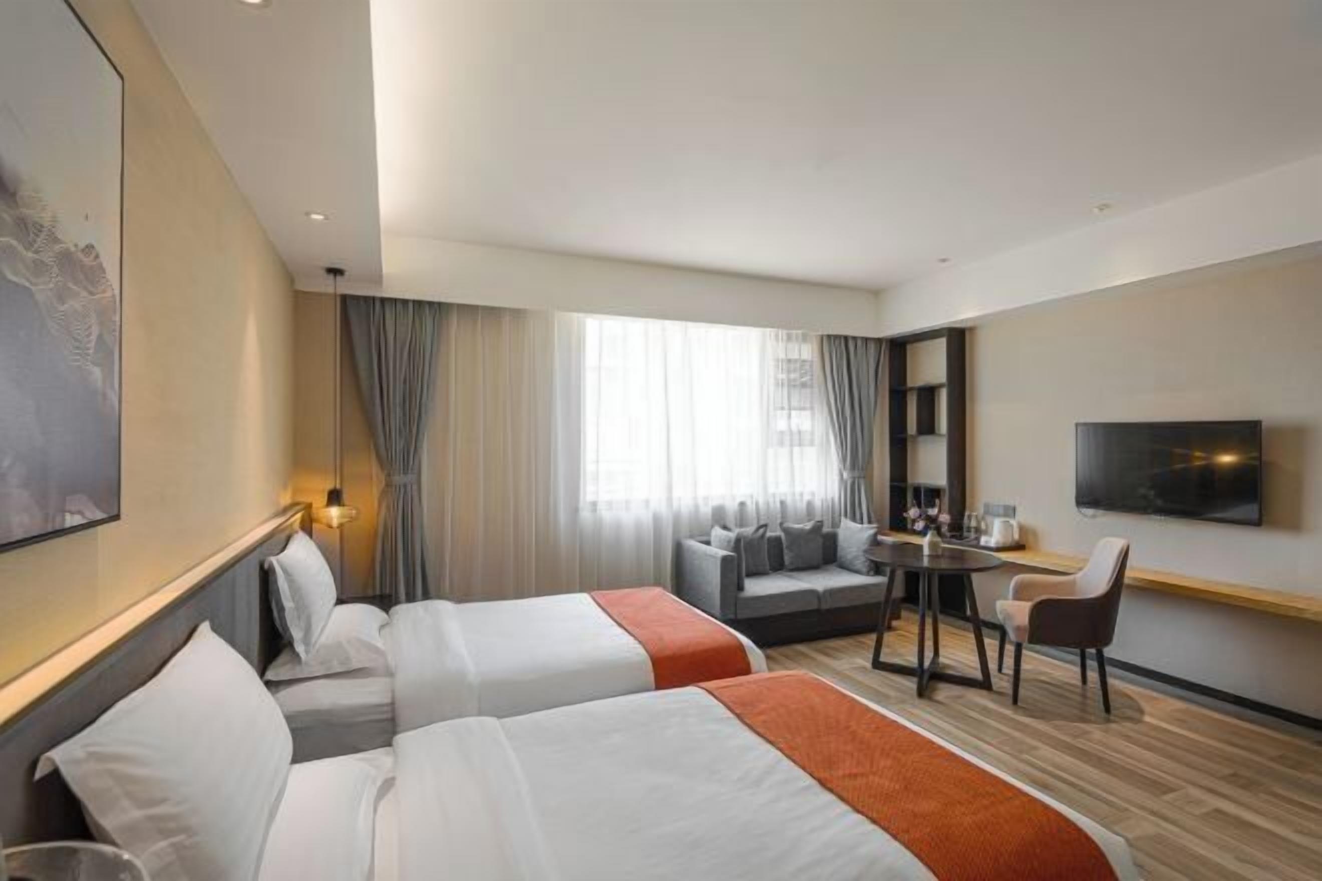 Habitación de hotel con dos camas, un sofá, una mesita, un televisor y un amplio ventanal con cortinas.