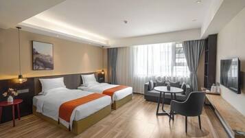 A hotel room with two beds, a sofa, a small table, and a TV.
