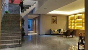 Un'ampia hall con una scalinata in marmo, un divano e una parete di scaffali illuminati.