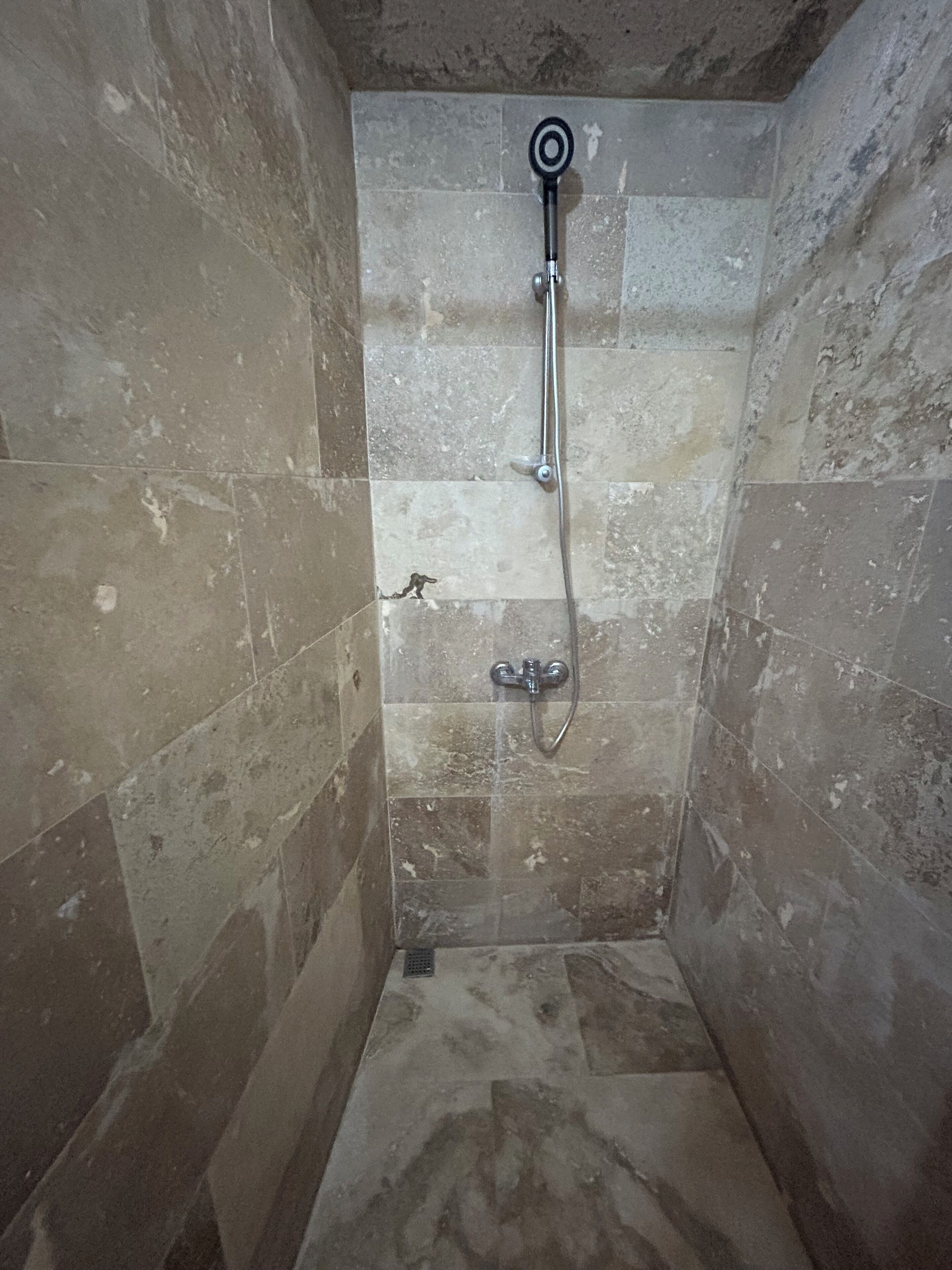 Un pequeño box de ducha con azulejos, un cabezal de ducha de mano y un grifo empotrado en la pared.