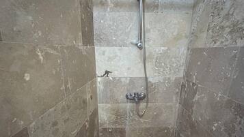 Un pequeño box de ducha con azulejos, un cabezal de ducha de mano y un grifo empotrado en la pared.