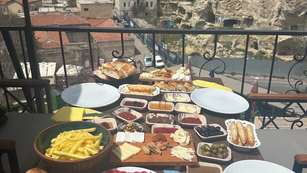 A table with various food items and a view of a mountainous town. - Bellavista Stone House (Urgup)