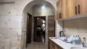 A narrow hallway leading to a bedroom with a bed, a wooden cabinet with a sink, and a patterned rug. - Bellavista Stone House (Urgup)