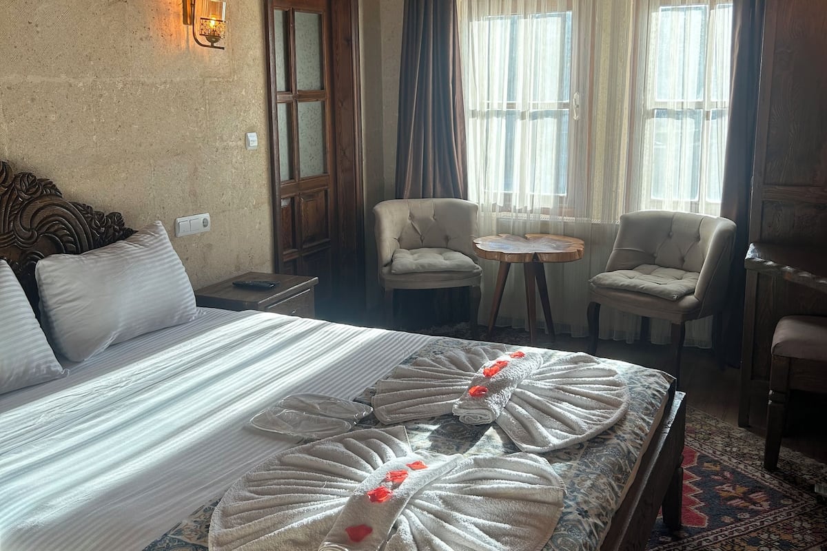 Habitació d'hotel amb un llit gran, dues butaques, una taula petita i un armari de fusta.