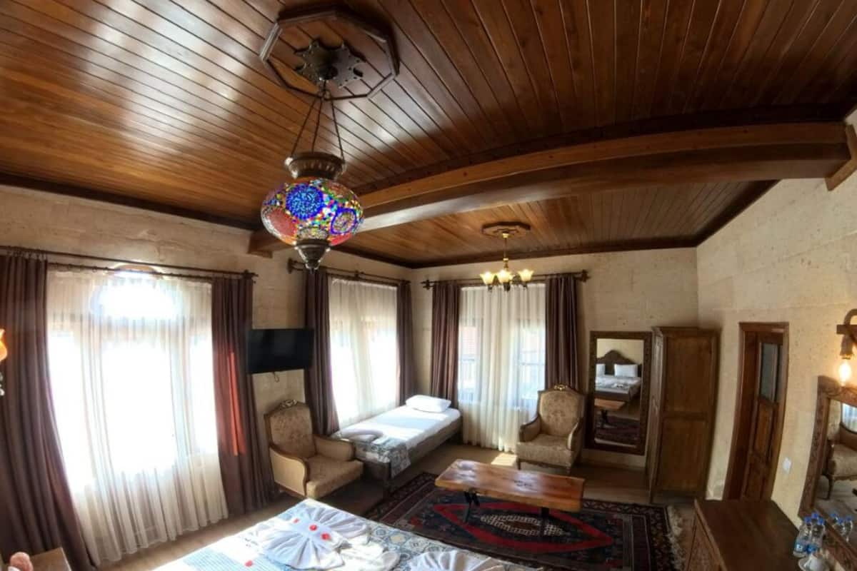 Una habitació amb sostre de fusta, un llit amb col·cha estampada, una cadira, una taula petita i un mirall.