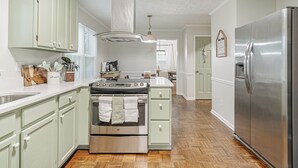 Eine Küche mit hellgrünen Schränken, einem Edelstahlkühlschrank und einem Holzboden im Fischgrätmuster.