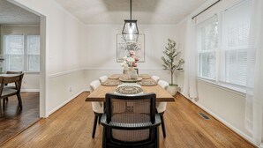 Ein Esszimmer mit Holztisch, weißen Wänden und einer Pendelleuchte.