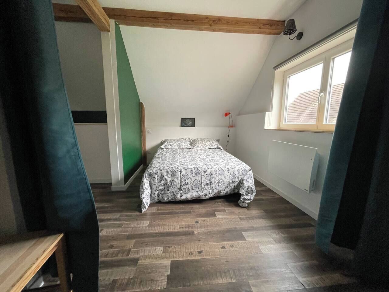Une chambre à coucher avec un lit, un plancher en bois, une fenêtre et un plafond en pente.