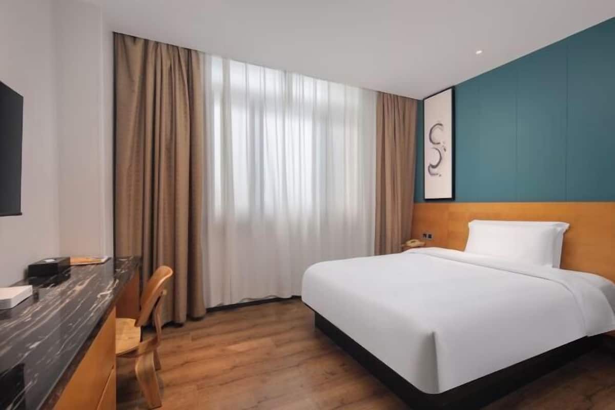 Une chambre d’hôtel avec un lit, un bureau, une chaise et une fenêtre avec des rideaux.