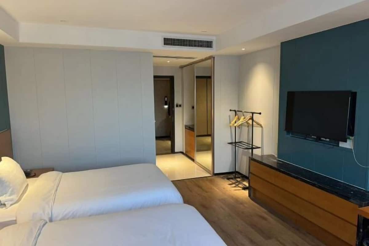 Une chambre d’hôtel avec deux lits, une télévision, un plancher en bois et une vue sur le couloir.