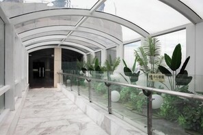 A corridor with a glass railing, marble flooring, and indoor plants. - GELI Hotel (Hongqiao Airport Wuzhong Road) (Shanghai)
