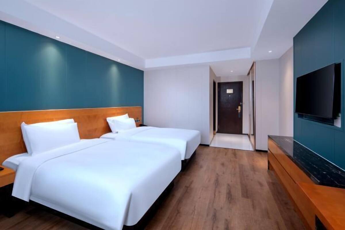 Une chambre d’hôtel avec deux lits, une télévision et un banc en bois.
