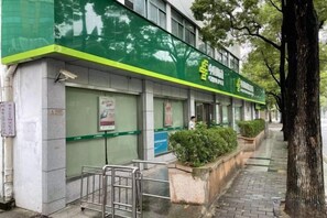 A building with a green facade, a gated entrance, and a sidewalk with planters. - GELI Hotel (Hongqiao Airport Wuzhong Road) (Shanghai)